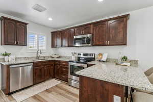 Kitchen with appliances with stainless steel finishes, a peninsula, light stone counters, light wood-style flooring, and recessed lighting