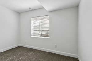 Spare room featuring dark colored carpet and baseboards
