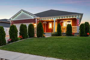 View of front of house featuring an attached garage, covered porch, stone siding, and a front lawn