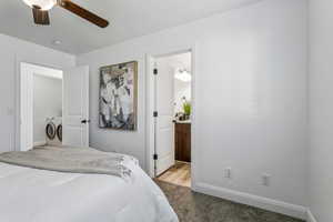 Bedroom with washer and clothes dryer, ensuite bathroom, light carpet, and ceiling fan