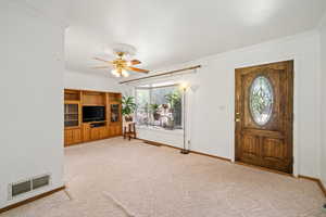 Foyer with ornamental molding, light colored carpet, and a ceiling fan