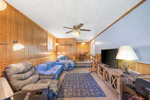 Living area featuring wooden walls, carpet floors, ceiling fan, and crown molding