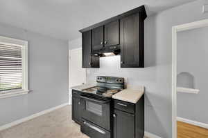 Kitchen with black range with electric stovetop, under cabinet range hood, light countertops, and dark cabinetry