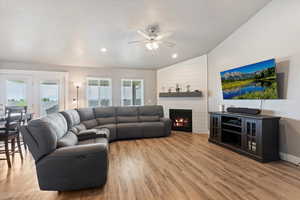 Living area with lofted ceiling, ceiling fan, wood finished floors, a large fireplace, and healthy amount of natural light