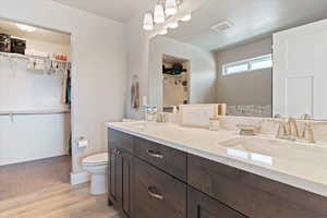 Bathroom with double vanity, a walk in closet, and wood finished floors
