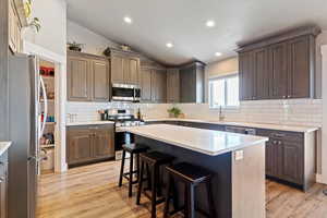 Kitchen featuring appliances with stainless steel finishes, lofted ceiling, a breakfast bar area, light wood finished floors, and light countertops