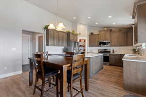 Kitchen with stainless steel appliances, backsplash, light countertops, a chandelier, and light wood-style flooring