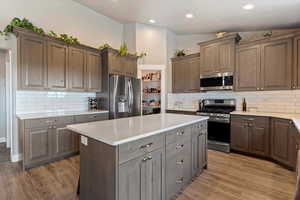 Kitchen featuring appliances with stainless steel finishes, light wood-style floors, a center island, decorative backsplash, and recessed lighting
