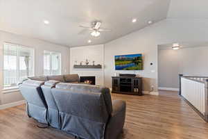 Living area featuring vaulted ceiling, ceiling fan, wood finished floors, a large fireplace, and recessed lighting
