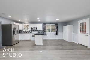 Kitchen with stainless steel appliances, dark countertops, a wainscoted wall, light wood finished floors, and white cabinetry