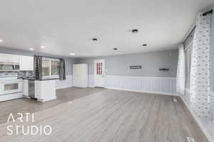 Kitchen featuring stainless steel appliances, a peninsula, wainscoting, light wood finished floors, and dark countertops