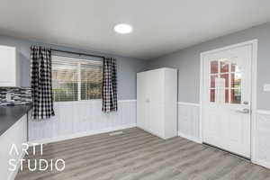 Unfurnished dining area featuring a wainscoted wall, light wood finished floors, and healthy amount of natural light