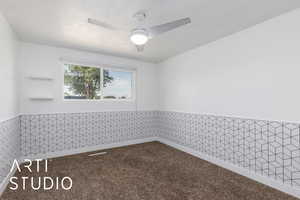 Carpeted empty room featuring wainscoting and a ceiling fan
