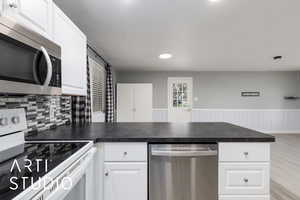Kitchen featuring appliances with stainless steel finishes, a peninsula, white cabinets, dark countertops, and recessed lighting