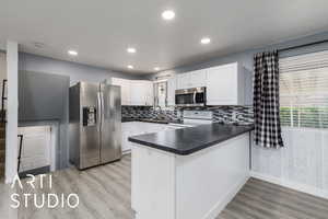 Kitchen with appliances with stainless steel finishes, a peninsula, dark countertops, light wood-type flooring, and white cabinetry