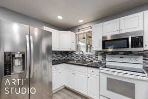 Kitchen featuring stainless steel appliances, dark countertops, white cabinetry, backsplash, and recessed lighting
