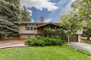 View of front facade with driveway, a front yard, a chimney, and a garage