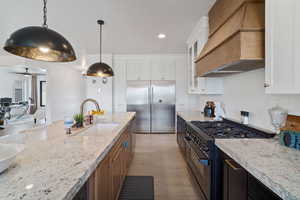 Kitchen featuring premium range hood, high quality appliances, glass insert cabinets, light stone counters, and white cabinets