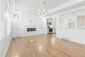 Unfurnished living room with a chandelier, a glass covered fireplace, light wood-style flooring, and recessed lighting