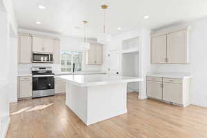 Kitchen with stainless steel appliances, light countertops, light wood-type flooring, a kitchen island, and hanging light fixtures