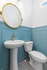 Half bathroom with a decorative wall, a wainscoted wall, and tile patterned floors
