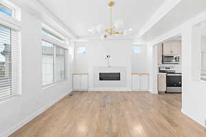 Unfurnished living room featuring a glass covered fireplace, light wood finished floors, a chandelier, recessed lighting, and a tray ceiling