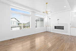 Unfurnished living room featuring a chandelier, a glass covered fireplace, light wood finished floors, and recessed lighting