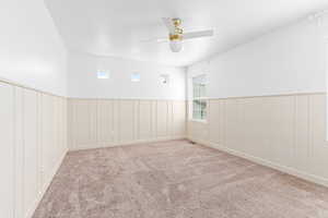 Empty room with a ceiling fan, carpet flooring, wainscoting, plenty of natural light, and a decorative wall