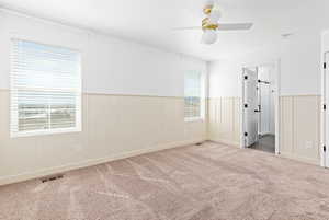 Unfurnished bedroom featuring carpet floors, a wainscoted wall, and a ceiling fan