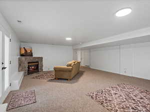 Carpeted living area featuring a stone fireplace and baseboards