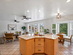 Kitchen with light tile patterned flooring, a center island, ceiling fan, light stone countertops, and a textured ceiling