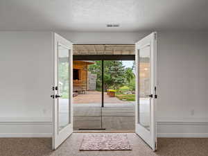 Doorway to outside featuring french doors, carpet flooring, and a textured ceiling