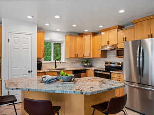Kitchen featuring appliances with stainless steel finishes, under cabinet range hood, a breakfast bar, tasteful backsplash, and recessed lighting