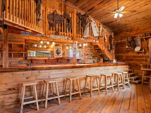 Bar area featuring wooden walls, wood ceiling, hardwood / wood-style floors, and a ceiling fan