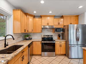 Kitchen featuring appliances with stainless steel finishes, under cabinet range hood, tasteful backsplash, light tile patterned flooring, and recessed lighting