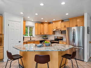 Kitchen with stainless steel appliances, under cabinet range hood, light tile patterned floors, backsplash, and recessed lighting