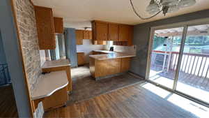 Kitchen featuring brown cabinetry, a peninsula, dark wood finished floors, light countertops, and a textured ceiling
