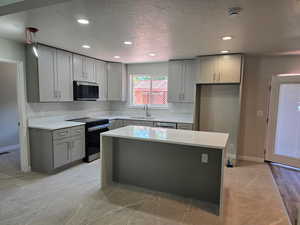 Kitchen featuring appliances with stainless steel finishes, gray cabinets, recessed lighting, a kitchen island, and light countertops