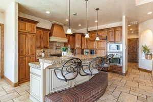 Kitchen featuring a kitchen breakfast bar, stone tile floors, brown cabinetry, pendant lighting, and recessed lighting