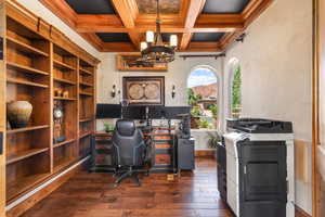Office space featuring dark wood-style floors, coffered ceiling, hanging lights, and crown molding