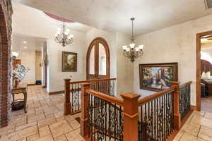 Hallway featuring stone tile flooring, a chandelier, and an upstairs landing