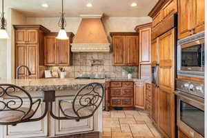 Kitchen featuring brown cabinetry, built in appliances, tasteful backsplash, custom range hood, and recessed lighting