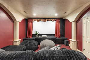 Home theater room with arched walkways, decorative columns, carpet, and recessed lighting