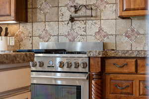 Kitchen view of stainless steel range with gas cooktop, wood finish cabinets, tasteful backsplash, and pot filler