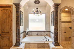 Full bathroom featuring ornate columns, tiled shower, a tub with jets, and hanging lights