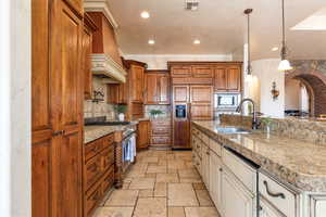 Kitchen with pendant lighting, built in appliances, stone tile flooring, dual tone cabinetry, and arched walkways
