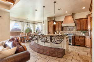 Kitchen featuring a kitchen bar, brown cabinets, decorative light fixtures, a center island with sink, and recessed lighting