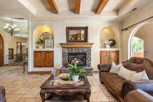 Living room with stone tile flooring, hanging lights, beamed ceiling, a stone fireplace, and arched walkways