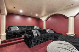 Carpeted cinema room featuring ornate columns, recessed lighting, and arched walkways