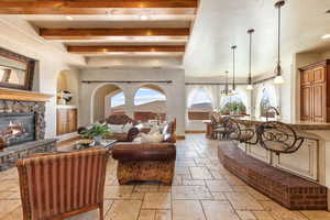 Living area with stone tile floors, a fireplace, beamed ceiling, and hanging lights